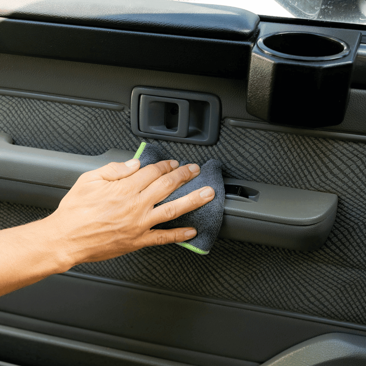 A man holding a black and green microfibre cloth, wiping a car interior.